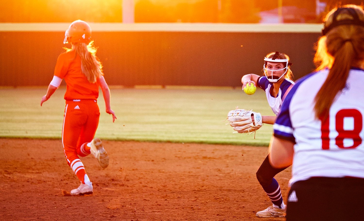Lindsey Hornaday makes a play to Reiny Luman at first base as Emily Wiley makes her way to second, into the setting sun. [see more fields of view]